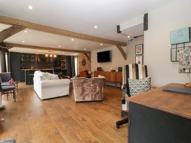 An open plan living room and kitchen with wooden beams white sofa striped armchair wooden floor and wall mounted tv at The Courtyard - Hilltop Barn Winterborne Zelston near Wareham