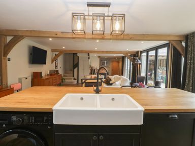 A kitchen island with a double sink and black cabinets overlooking a living area with wooden beams at The Courtyard - Hilltop Barn in Winterborne Zelston near Wareham