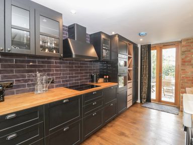 A kitchen with black cabinets wooden countertops glass door cupboards and a door to the outside at The Courtyard - Hilltop Barn Winterborne Zelston near Wareham