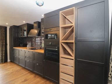 A kitchen with black cabinets wooden countertops built in oven and microwave wooden open shelves and drawers at The Courtyard - Hilltop Barn Winterborne Zelston near Wareham