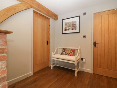 A hallway with wooden doors a white bench with a cushion and a framed picture on the wall at The Courtyard - Hilltop Barn in Winterborne Zelston near Wareham