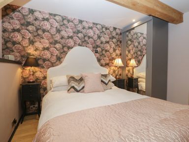 A bedroom with a bed pillows and lamps against a floral wallpapered wall at The Courtyard - Hilltop Barn Winterborne Zelston near Wareham