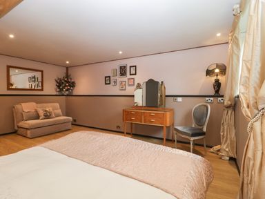 A bedroom with a bed a wooden dressing table and chair a small sofa and a large mirror at The Courtyard - Hilltop Barn Winterborne Zelston near Wareham