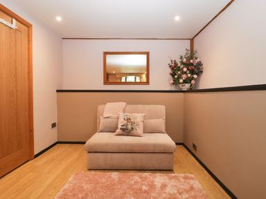 A small beige sofa with cushions and a throw in a room with wooden floor a pink rug a wooden door a wall mirror and a floral arrangement at The Courtyard - Hilltop Barn Winterborne Zelston near Wareham