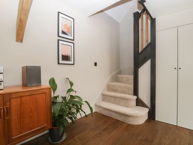 A hallway with carpeted stairs wooden floor cabinet with speaker and plant at The Courtyard - Hilltop Barn Winterborne Zelston near Wareham