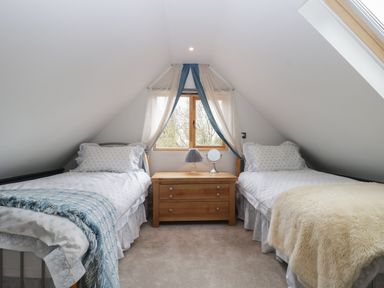 A bedroom with two single beds separated by a wooden nightstand with a lamp and mirror at The Courtyard - Hilltop Barn Winterborne Zelston near Wareham