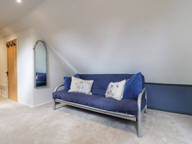 A room with a blue futon sofa and pillows beside a wall mirror and wooden door at The Courtyard - Hilltop Barn in Winterborne Zelston near Wareham