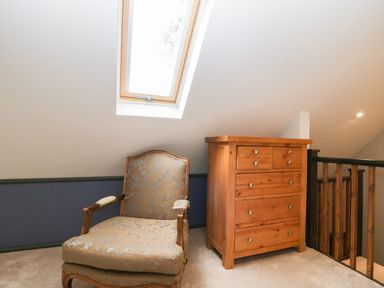 An armchair and wooden chest of drawers under a skylight in a carpeted loft space at The Courtyard - Hilltop Barn in Winterborne Zelston near Wareham