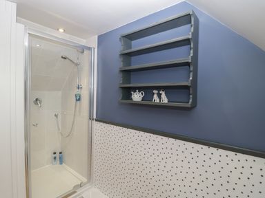 A bathroom with a glass shower enclosure and a wall-mounted shelf with decorative items at The Courtyard - Hilltop Barn Winterborne Zelston near Wareham