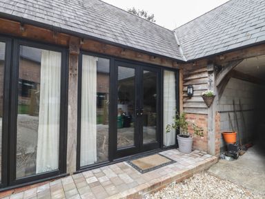 An exterior patio with glass doors and potted plants at The Courtyard - Hilltop Barn in Winterborne Zelston near Wareham