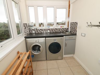 A utility room with a washing machine dryer cabinet sink tiled floor and windows at Windy Ridge in Trearddur Bay