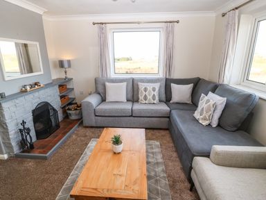 A living room with a gray sectional sofa wooden coffee table and a fireplace at Windy Ridge in Trearddur Bay