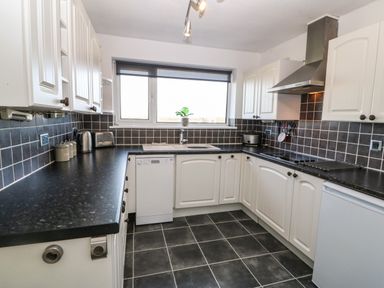 A kitchen with white cabinets black countertops and tiled floor at Windy Ridge in Trearddur Bay