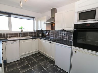 A kitchen with white cabinets black tiled backsplash and appliances at Windy Ridge in Trearddur Bay