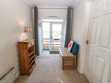 A narrow room with a wooden shelf and lamp on the left and a wooden bench with cushions on the right at Windy Ridge in Trearddur Bay