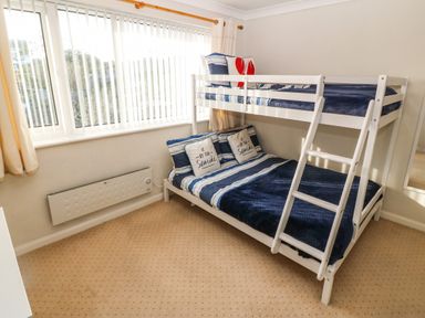 A bedroom with a white bunk bed striped bedding and a window with vertical blinds at Windy Ridge in Trearddur Bay