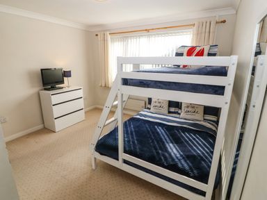 A bedroom with a bunk bed and a chest of drawers with a TV and lamp at Windy Ridge in Trearddur Bay
