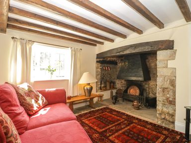 A living room with wooden ceiling beams a stone fireplace a red sofa and a lamp on a wooden bench at Field View in Curland near Taunton