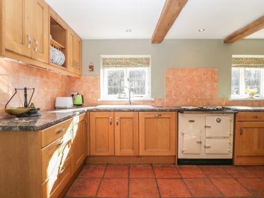 A kitchen with wooden cabinets tiled walls and floor with a stove and a sink under windows at Field View in Curland near Taunton