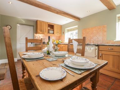 A kitchen with wooden cabinets a dining table set with plates glasses and cutlery at Field View in Curland near Taunton