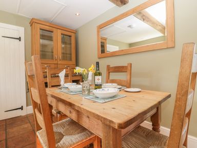 A dining room with a wooden table set for four with bowls and a bottle of wine and a wooden cabinet at Field View in Curland near Taunton
