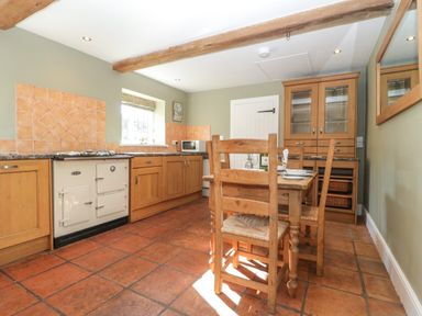 A kitchen with wooden cabinets a dining table and chairs and a white stove at Field View in Curland near Taunton