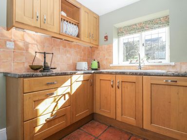 A kitchen with wooden cabinets a countertop a sink under a window and small appliances at Field View in Curland near Taunton