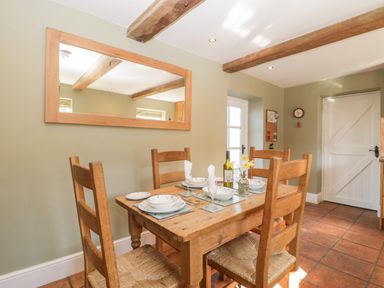 A dining area with a wooden table set for four and a large wall mirror at Field View in Curland near Taunton
