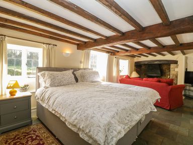 A bedroom with a large bed and bedside table next to a red sofa facing a fireplace at Field View in Curland near Taunton