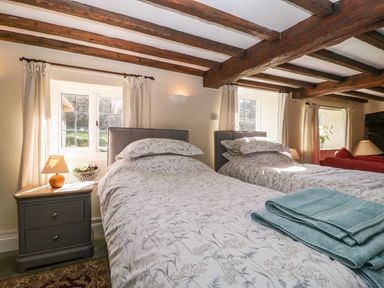 A bedroom with two single beds side by side with floral bed linens and towels on one bed next to windows and bedside tables at Field View in Curland near Taunton