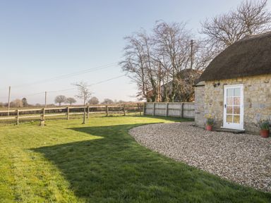 A stone cottage with a thatched roof and gravel path surrounded by a grassy yard and wooden fence at Field View in Curland near Taunton