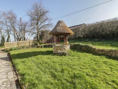 A garden with grass a stone well with a thatched roof and a stone path at Field View in Curland near Taunton