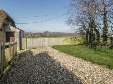A gravel driveway next to a stone building with a thatched roof and a wooden fence at Field View in Curland near Taunton