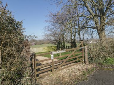A wooden gate with a sign reading Forest Farm Cottage opening to a gravel path and fields at Field View in Curland near Taunton