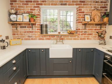 A kitchen with dark cabinets farmhouse sink and exposed brick walls at Pumphouse Cottage in Uffculme