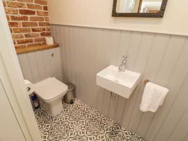A small bathroom with a toilet a small sink a towel on a ring and patterned floor tiles at Pumphouse Cottage in Uffculme