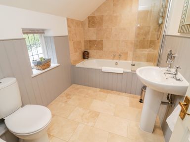 A bathroom with a toilet sink bathtub with shower and a window with a basket on the sill at Pumphouse Cottage in Uffculme