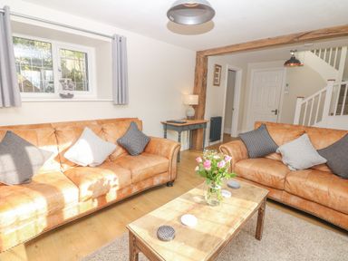 A living room with two brown leather sofas a wooden coffee table with flowers a small desk lamp and a staircase at Pumphouse Cottage in Uffculme