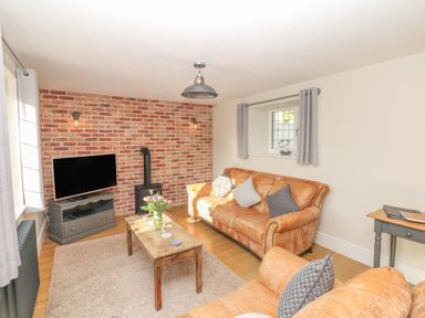 A living room with leather sofas a wooden coffee table and a television on a stand at Pumphouse Cottage in Uffculme