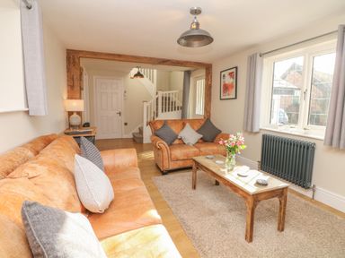 A living room with leather sofas wooden coffee table flowers and a window at Pumphouse Cottage in Uffculme