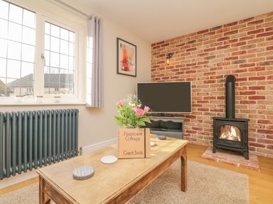 A living room with a wooden coffee table with flowers and a guest book a TV on a stand a fireplace and a window at Pumphouse Cottage in Uffculme