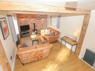 A living room with two orange sofas a wooden coffee table a TV a wood-burning stove and a side table with a lamp at Pumphouse Cottage in Uffculme