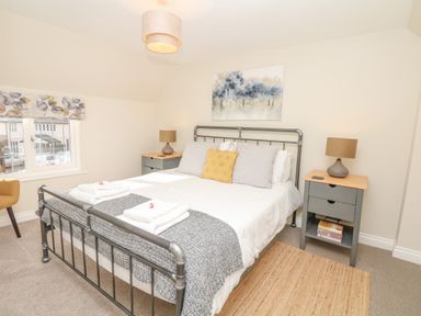 A bedroom with a metal bed frame two bedside tables with lamps and a window at Pumphouse Cottage in Uffculme