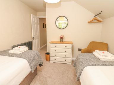 A bedroom with two beds a chest of drawers a round mirror and a chair at Pumphouse Cottage in Uffculme