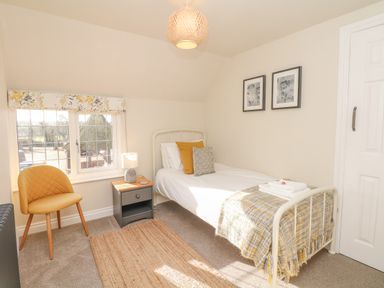 A bedroom with a single bed armchair side table and window at Pumphouse Cottage in Uffculme