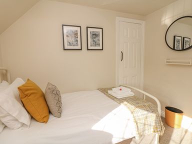 A bedroom with a bed with pillows and folded towels on a blanket a door two framed pictures a round mirror and a waste bin at Pumphouse Cottage in Uffculme