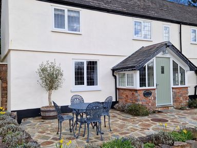 A patio with a metal table and four chairs outside a cottage with white walls and a green door at Pumphouse Cottage in Uffculme