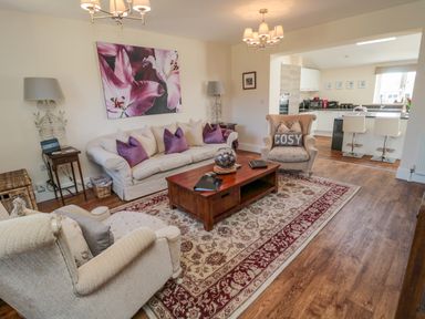 A living room with beige sofas purple cushions a wooden coffee table and lamps at Cushat House Stamford near Embleton