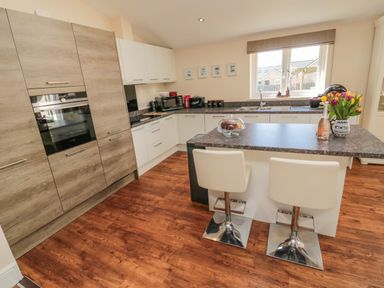 A kitchen with an island counter and two chairs a window above the sink and wooden and white cabinets at Cushat House Stamford near Embleton