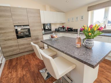 A kitchen with an island countertop two chairs and a vase of tulips at Cushat House Stamford near Embleton